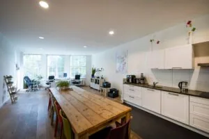 Moderne en lichte kantoorruimte aan de Nieuwezijds Voorburgwal met een lange houten tafel, keukenblok en werkplekken bij grote ramen.